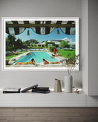 Framed photograph of a pool scene with people lounging, displayed on a wall above a shelf.