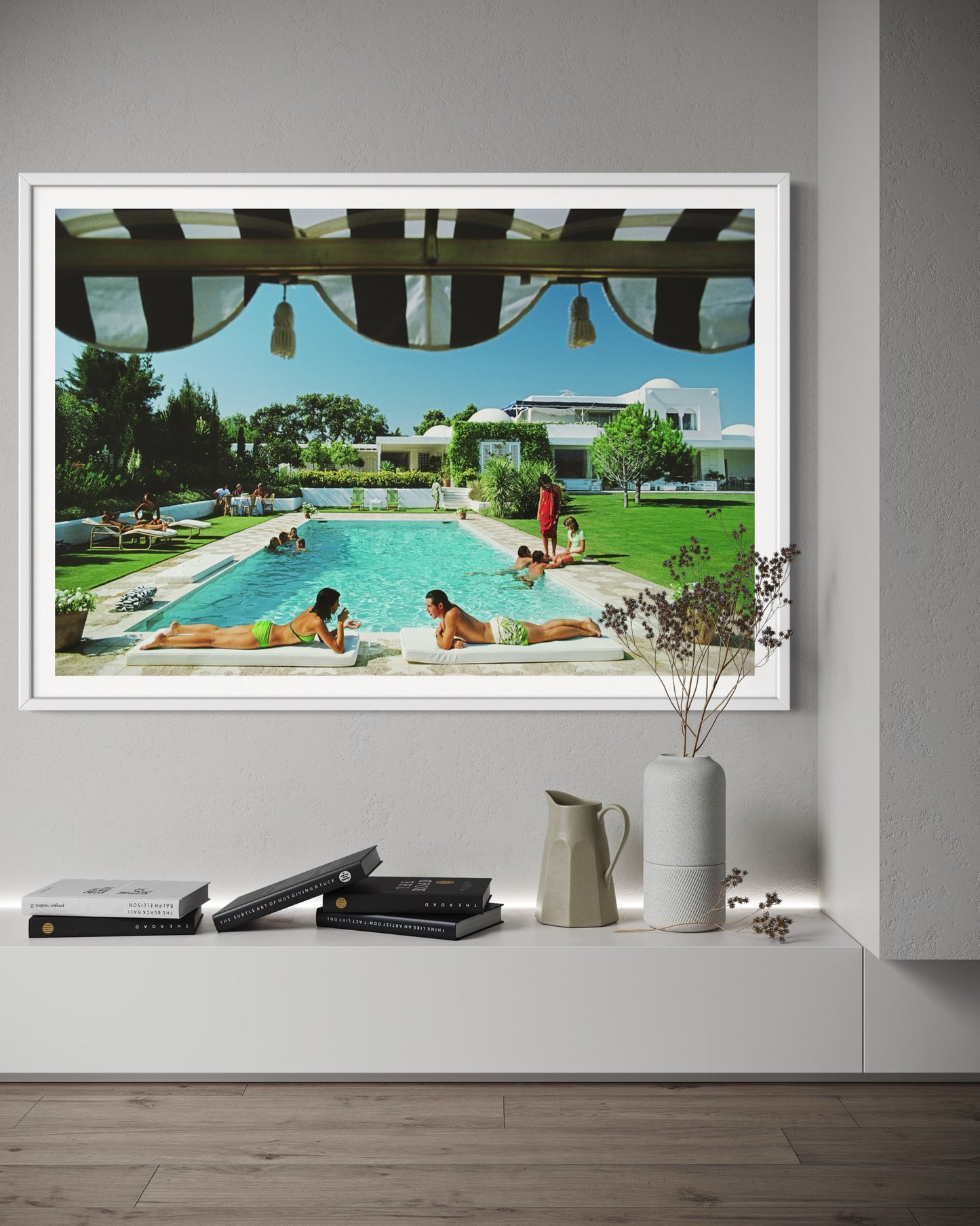 Framed photograph of a pool scene with people lounging, displayed on a wall above a shelf.