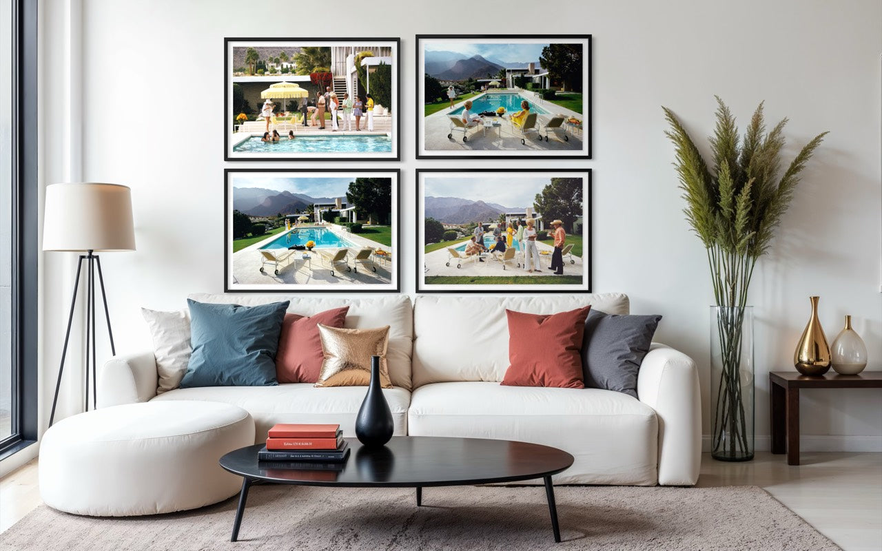 A styled living room featuring a white sectional sofa with accent pillows, a black coffee table, and a large wall art set consisting of four framed photographs of poolside scenes. The Picturalist Wall Art and Photography for Designed Interiors. Slim Aarons Collection, Poolside. Getty Images Gallery. 