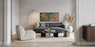 A modern living room scene featuring a dark gray fabric sofa, a cream boucle armchair, a black coffee table, and two framed abstract art prints hanging on the wall above the sofa.