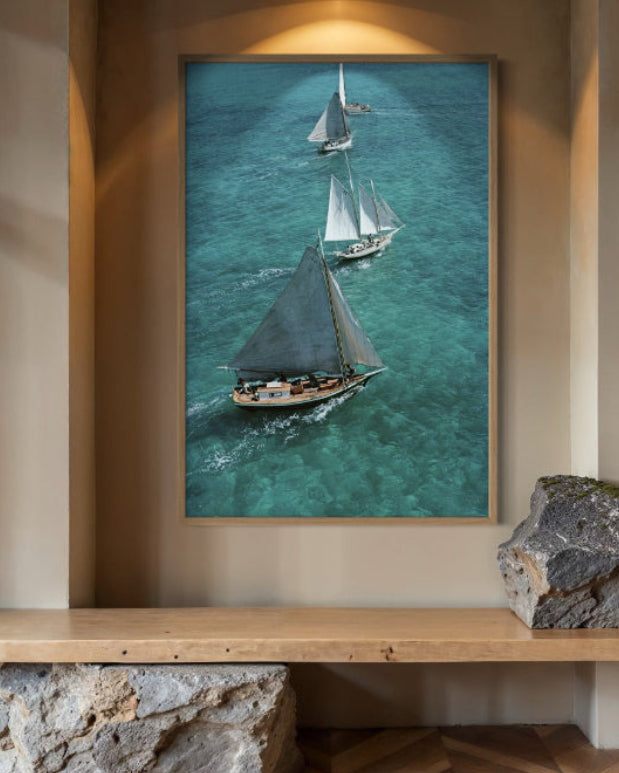Framed artwork of sailboats on a wall above a wooden shelf.