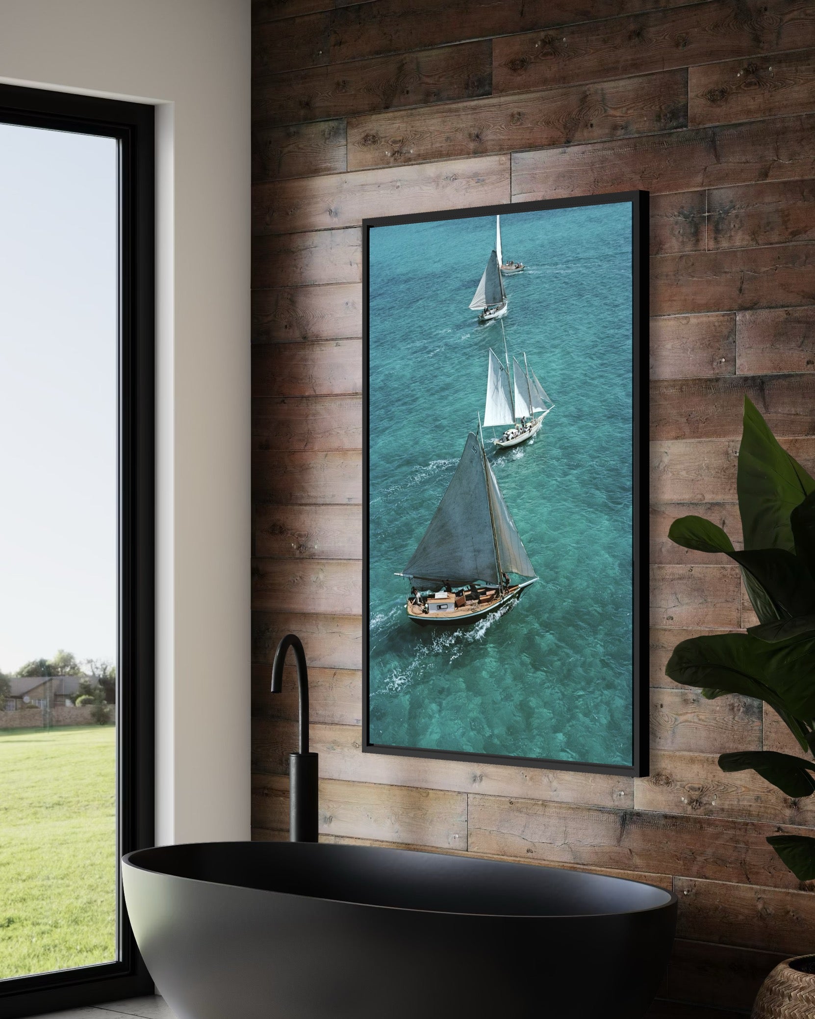 Framed artwork of sailboats on a wooden wall above a black freestanding bathtub.