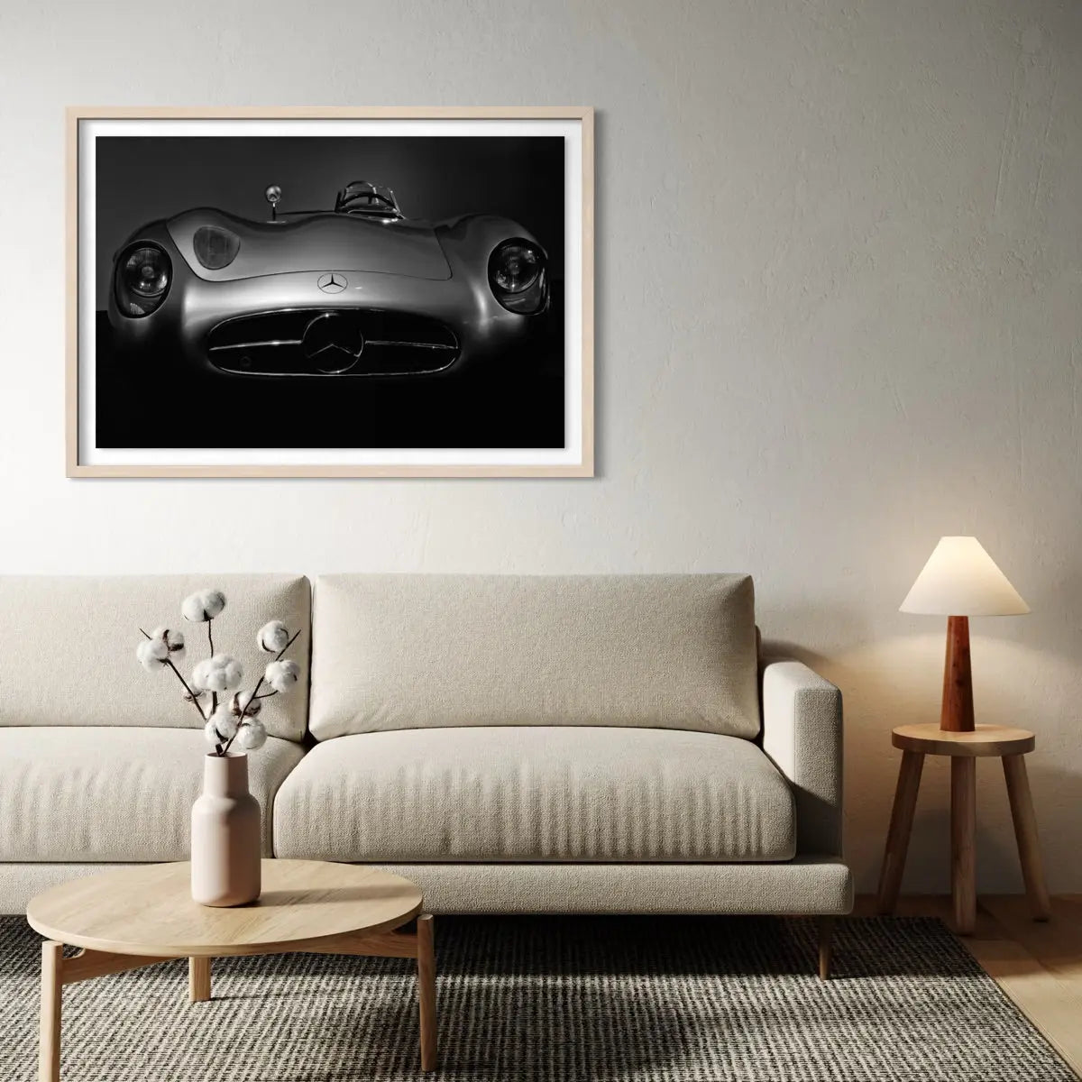 A framed black and white art print of a classic Mercedes-Benz sports car hanging on a light gray wall above a beige fabric sofa in a modern living room setting.