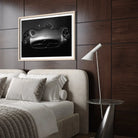 A framed black and white art print of a Mercedes-Benz sports car hanging on a dark wood-paneled wall above a bed in a modern bedroom setting.