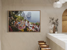 Framed artwork of a scenic coastal scene with people dining, displayed on a wall.