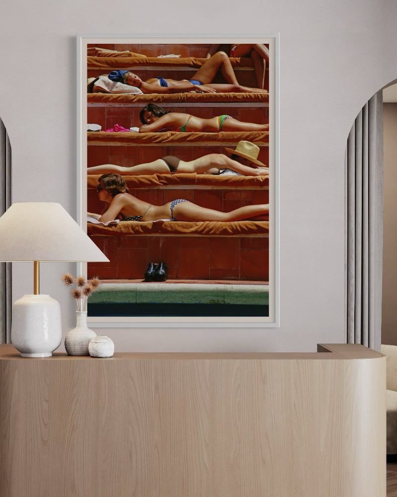 Modern interior with a framed artwork of women in swimsuits on a red background, a lamp, and a vase.