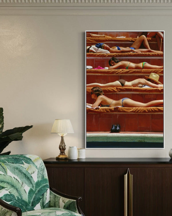 Framed artwork of people in a pool on a wall above a console table with decorative items.