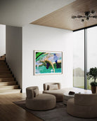 A framed abstract art print featuring a green and blue water scene with a horse, displayed on a white wall in a modern, sunlit living room with beige seating and a staircase.