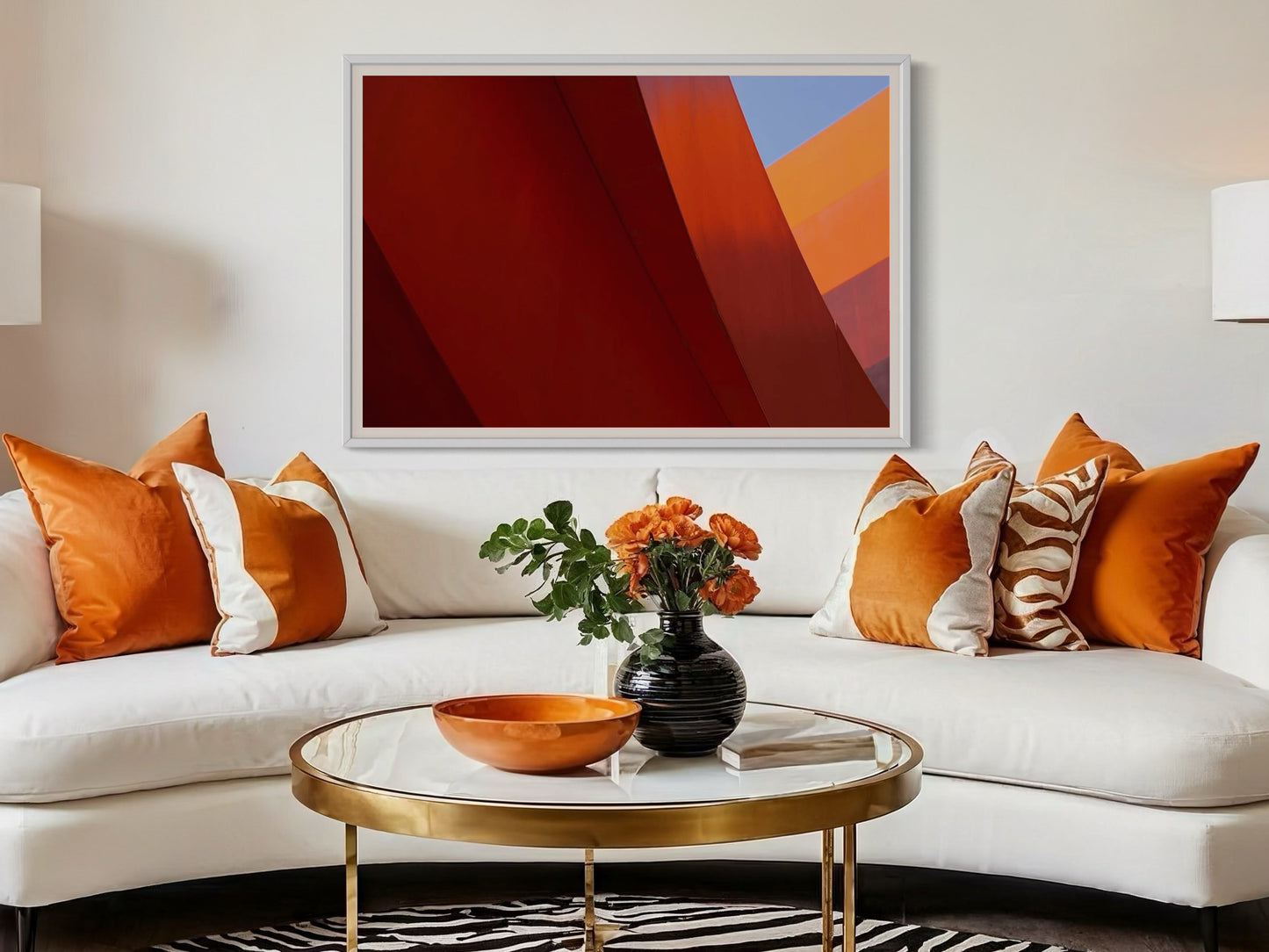 Modern living room with a white sofa, orange and white pillows, a gold coffee table, and abstract art on the wall.