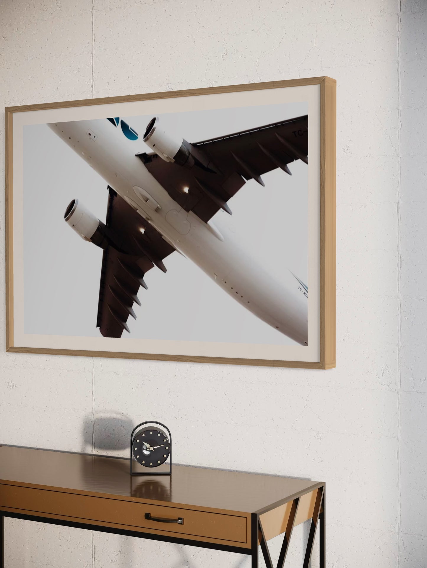 Framed photograph of an airplane on a wall above a console table with a clock.