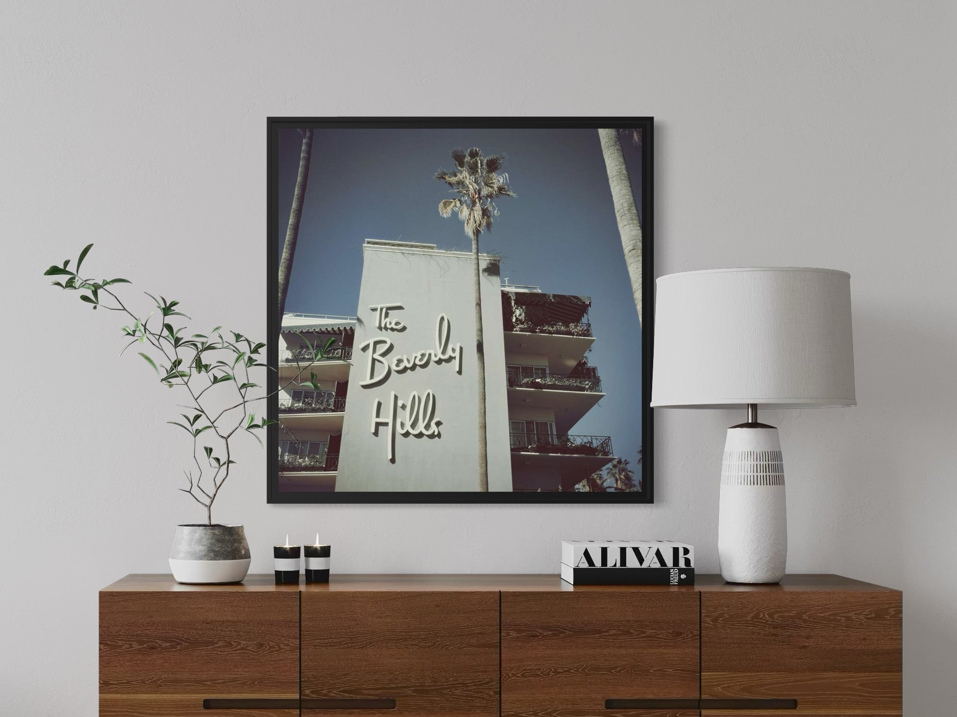 Framed artwork of a building with 'The Beach' sign on a wall above a wooden cabinet.