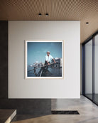 A framed art print depicting a gondola scene in Venice, displayed on a minimalist white wall inside a modern interior space with a slatted wood ceiling. The Picturalist Wall Art and Photography for Designed Interiors. Slim Aarons Collection, Venice. Getty Images Gallery. 