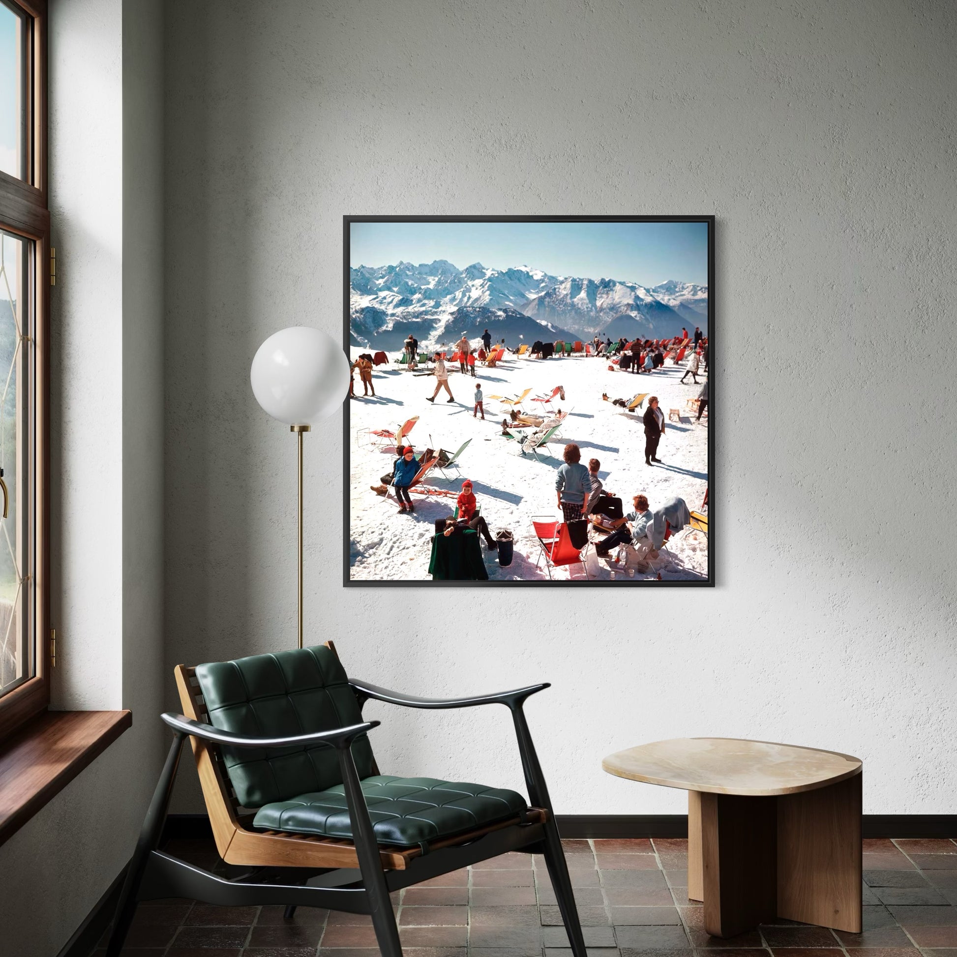 Framed photograph of a snowy mountain scene with people on a wall above a chair and table.