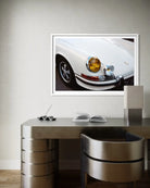 A framed art print of a white classic Porsche car, shown hanging on a light gray wall above a modern metallic desk and chair.
